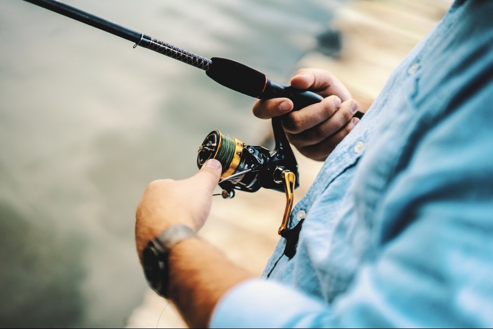 Man in a blue shirt holding a spinning reel.