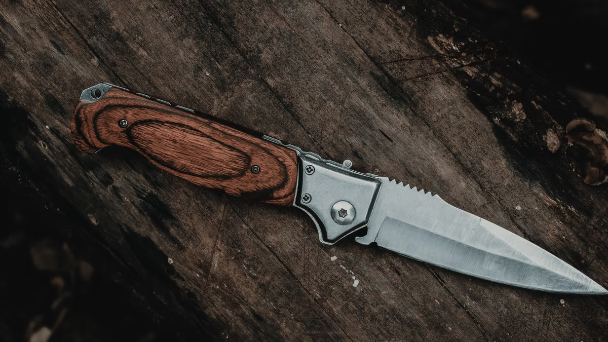 A pocket knife with a wooden handle on top of a wooden table.