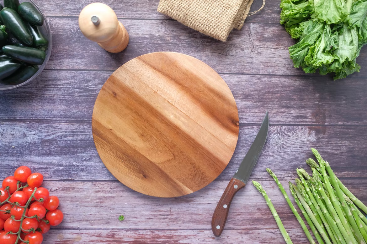 Cutting board on a table with a knife and vegetables.