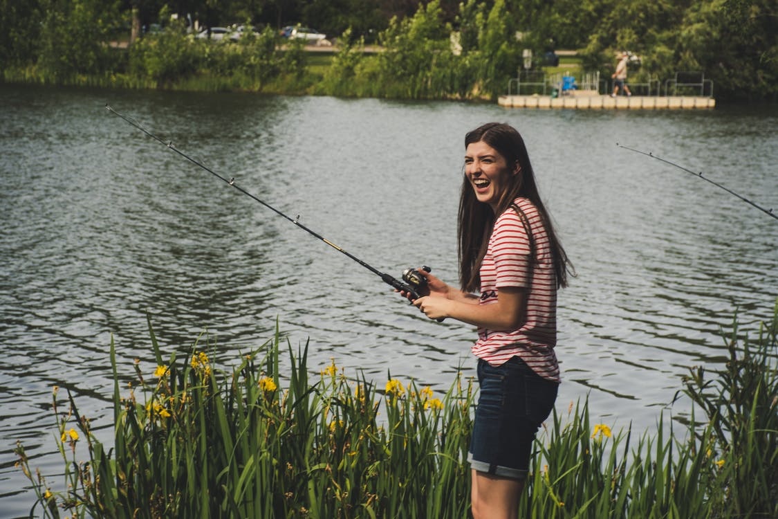 Lady next to a pond with a beginners fishing rod in her hand.