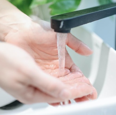 Lady washing hands in a kitchen sink with running water.