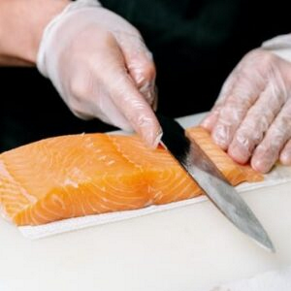 Man skinning salmon on cutting board with a fillet knife.