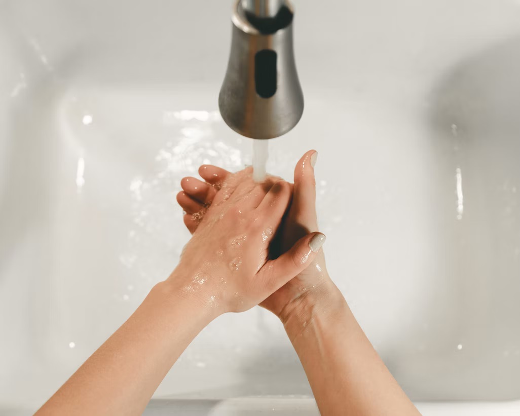 Person washing hands in clean sink under running water.