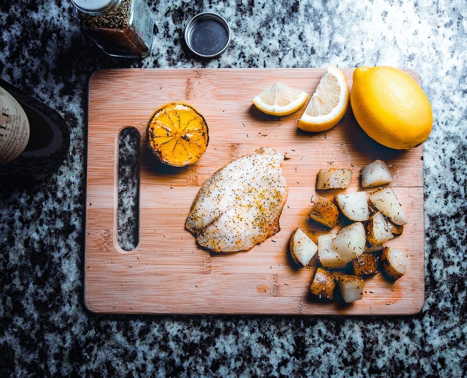 Raw seasoned fish on a cutting board with lemons and potatoes..