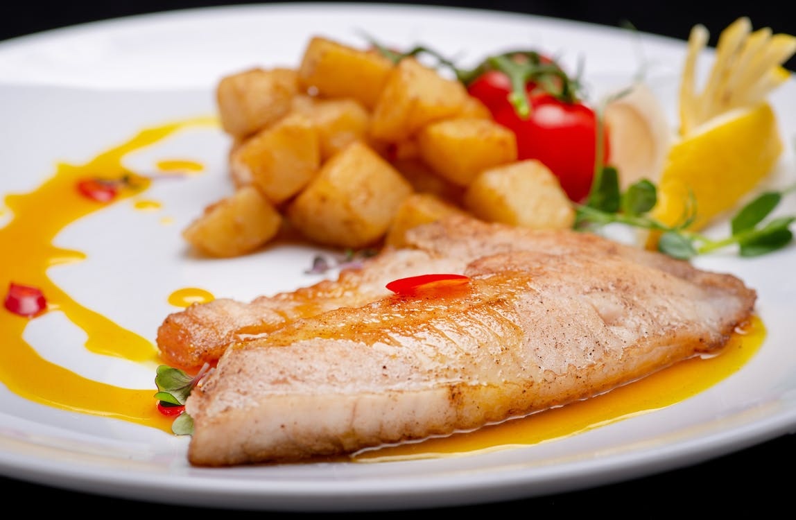 Skinned perch fillet baked on a plate with potatoes and cherry tomatoes.