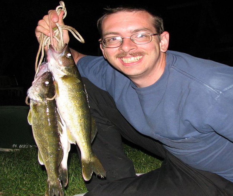 Man with stringer of walleye on water at night.