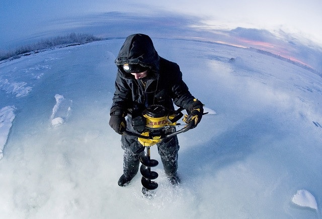isherman with auger drilling through the ice on a frozen lake.