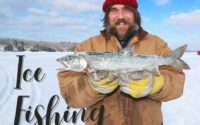 Man in ice fishing gear on a frozen lake holding a big salmon.