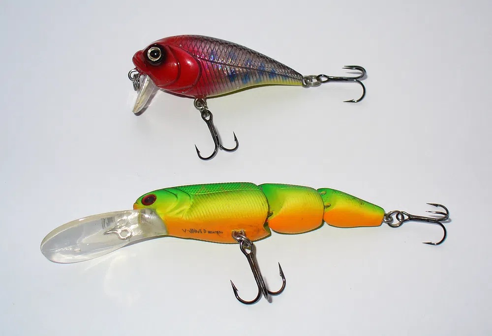 Green segmented swimbait and red crankbait on a white background.