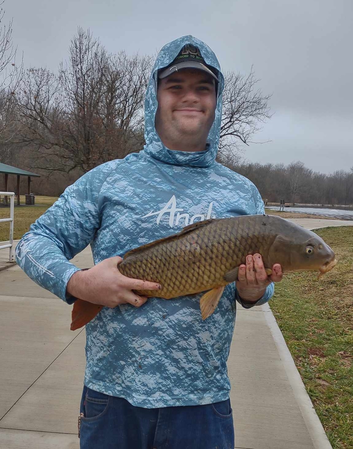 David Moore holding a common carp in front of a pond.