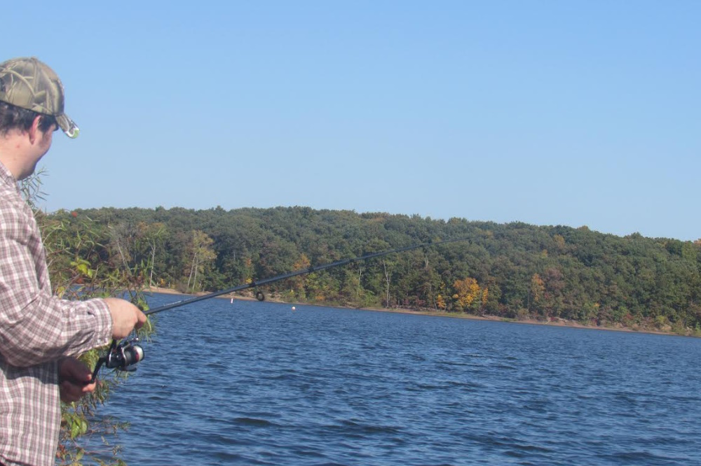 Man holding a spinning rod while fishing in water.