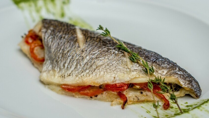 Smallmouth bass fish fillet on a plate with dill and peppers.